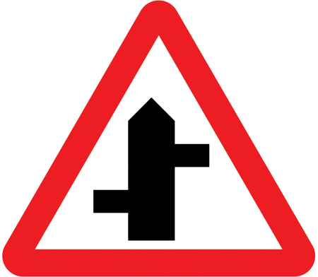 UK staggered junction warning sign: a red-bordered triangle showing side roads offset on either side.